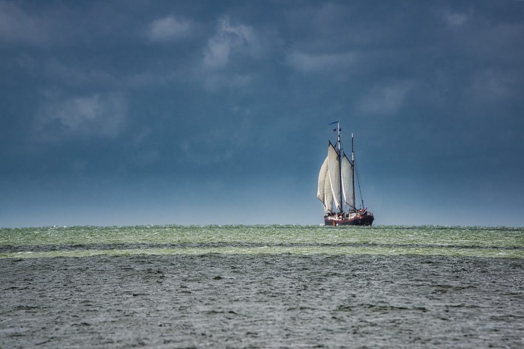 Landschaftsfotografie eines Segelschiffs auf dem Meer unter dunklem, dramatischem Himmel.