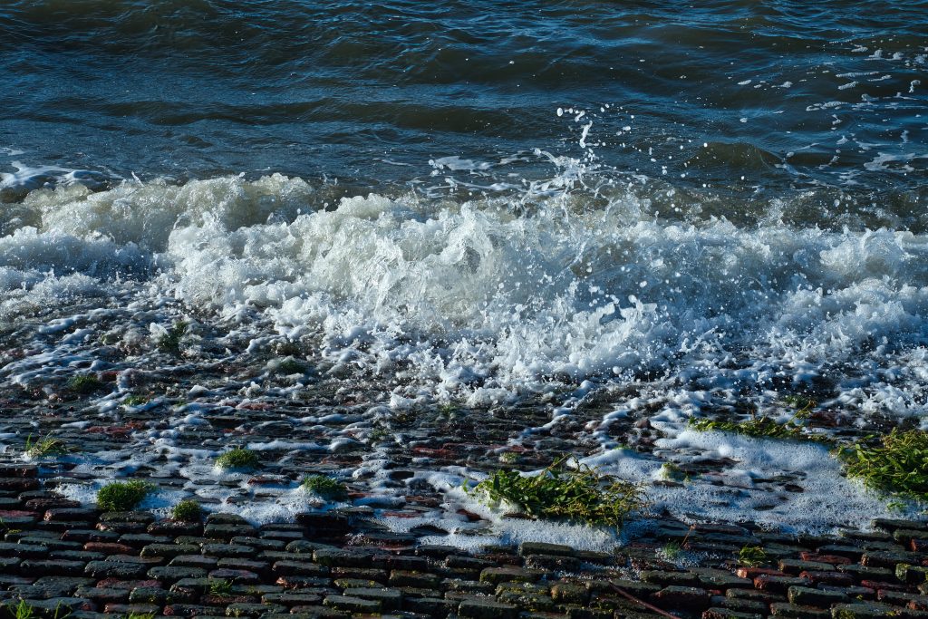 Wellen schlagen mit weißem Schaum gegen die gepflasterte Deichkante an der Nordsee.