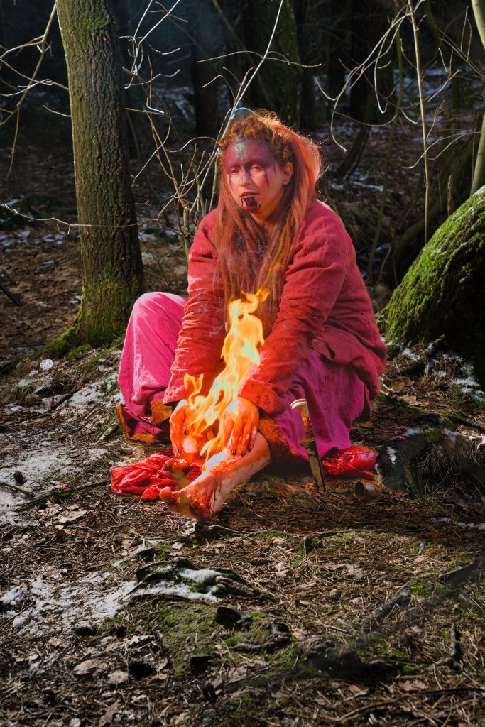 Inszenierte Fantasy Fotografie einer Person im Wald mit Feuer und dramatischer Beleuchtung.