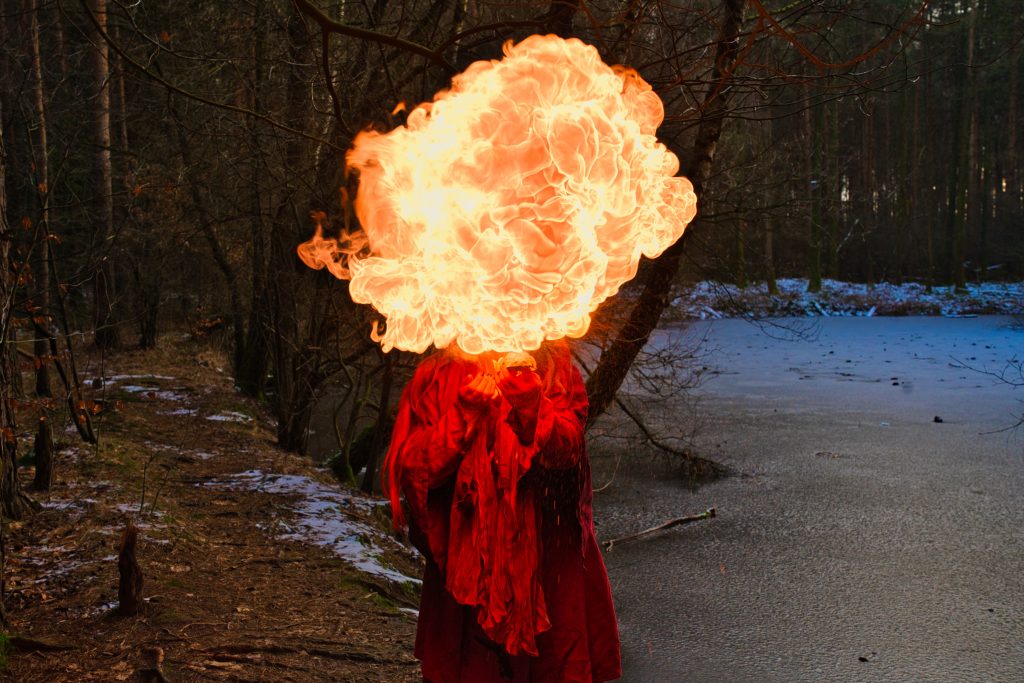 Künstlerische Fantasy Fotografie einer Person in rotem Gewand mit Feuerwolke im Wald.