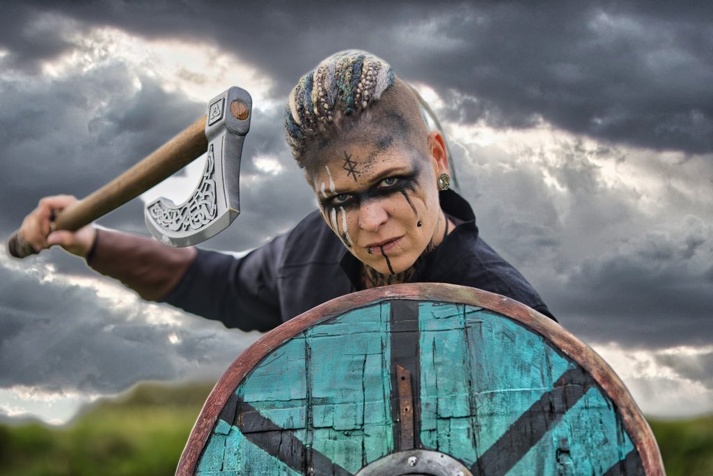 Fantasy Portrait einer Wikingerkriegerin mit Axt und Schild vor dramatischer Landschaft.