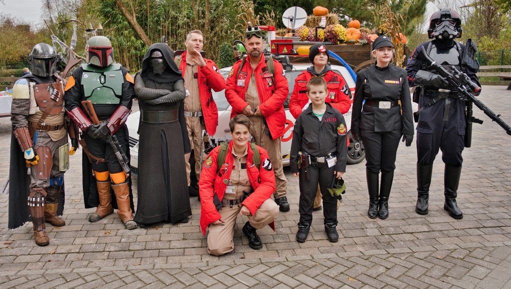 Gruppe von Cosplayern in Star-Wars- und Ghostbusters-Kostümen posiert im Freien vor einem dekorierten Auto.