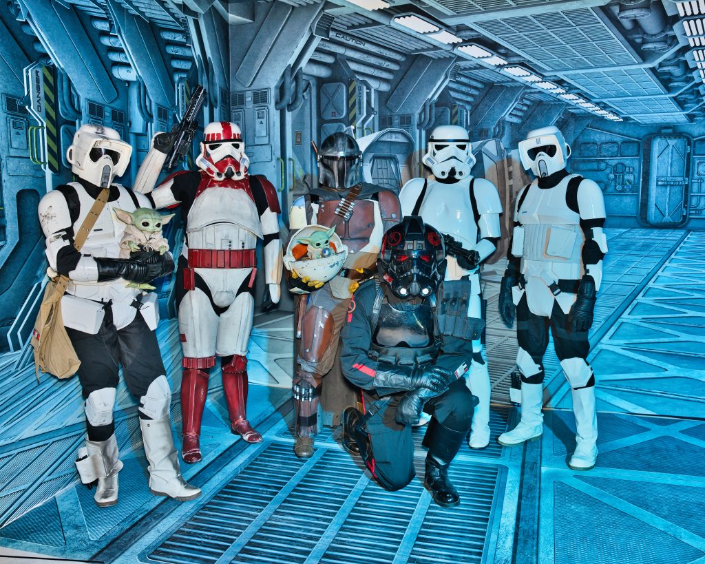 Gruppe von Star-Wars-Cosplayern in Rüstungen posiert in Raumschiff-Kulisse mit Grogu-Figuren.
