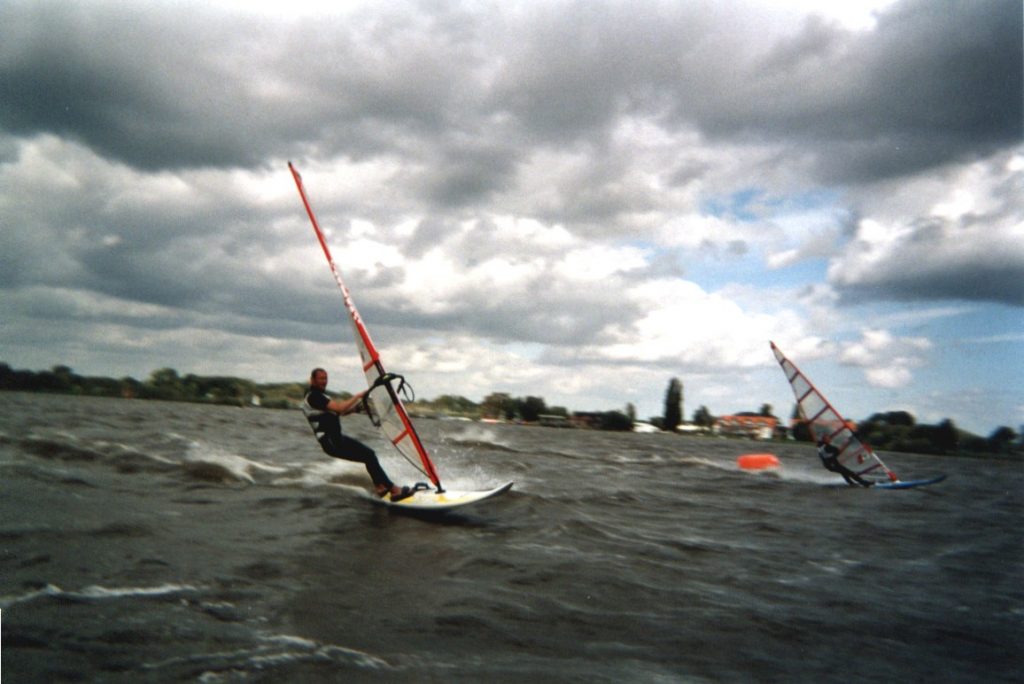 Zwei Windsurfer auf einem windigen See unter bewölktem Himmel in actionreicher Bewegung. Ein Beispiel für Sport Fotografie.