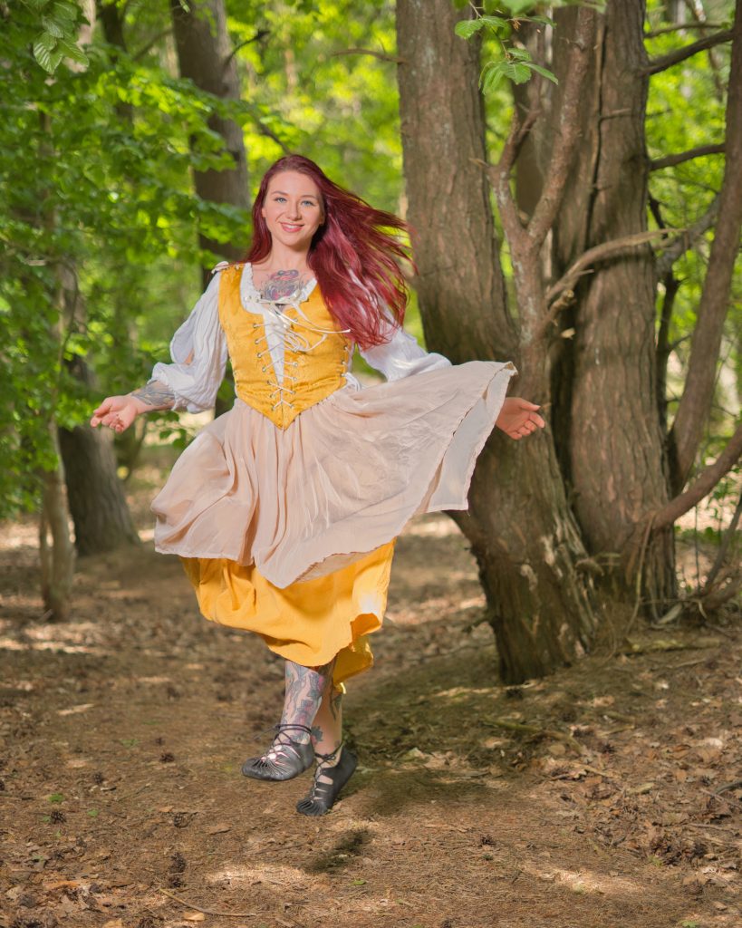 Fantasy Portrait einer fröhlichen Frau im mittelalterlichen Kleid beim Springen im Wald.