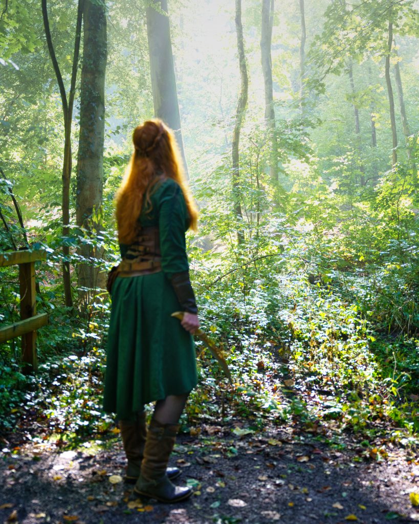 Fantasyfoto einer Waldläuferin mit roten Haaren und Dolch im Sonnenlicht – professionelle Fantasy Fotografie im mystischen Wald.