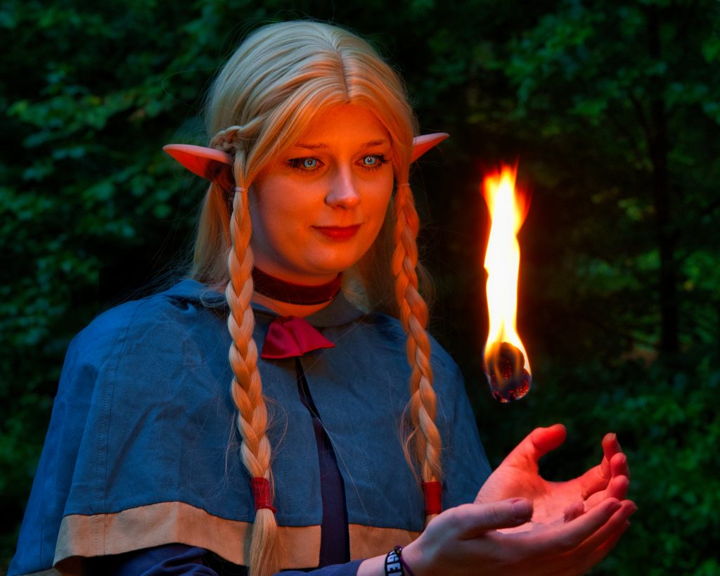 Fantasy Foto einer Elfenmagierin mit leuchtender Flamme in den Händen – professionelle Fantasy Fotografie im Wald.