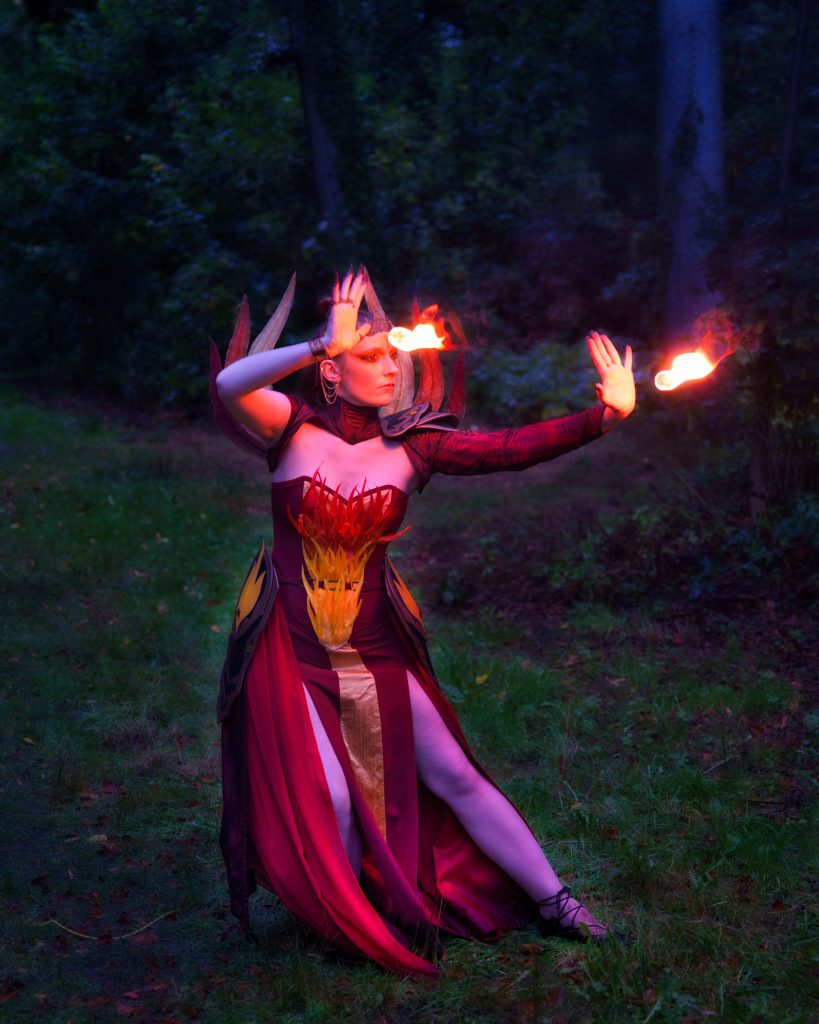 Fantasy Foto einer Magierin in rotem Kostüm, die Feuerkugeln im Wald kontrolliert – Fantasy Fotografie mit Lichteffekten.