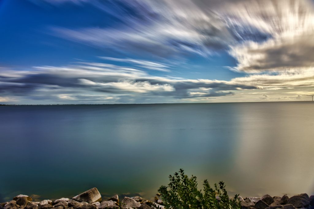 Landschaft Fotografie mit Langzeitbelichtung über ruhigem Meer und bewegten Wolken – stimmungsvolle Naturaufnahme mit sanftem Licht.