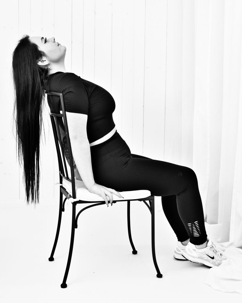 Schwarz-Weiß-Studioportrait einer Frau in sportlich-eleganter Pose auf einem Stuhl – künstlerische Porträt Fotografie.