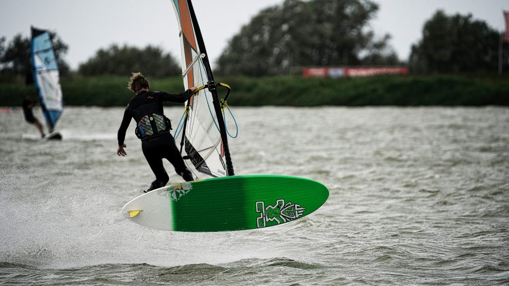 Windsurfer in Aktion hebt mit grünem Board vom Wasser ab – dynamische Sport Fotografie auf See.
