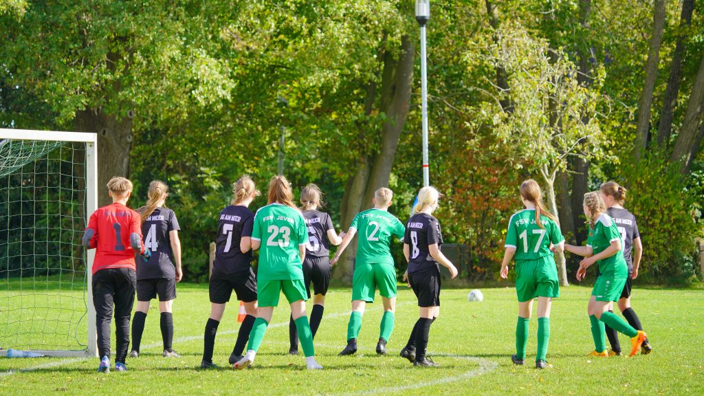 Sport Fotografie eines Frauenfußballspiels – Spielerinnen positionieren sich im Strafraum vor dem Tor, voller Konzentration und Bewegung.