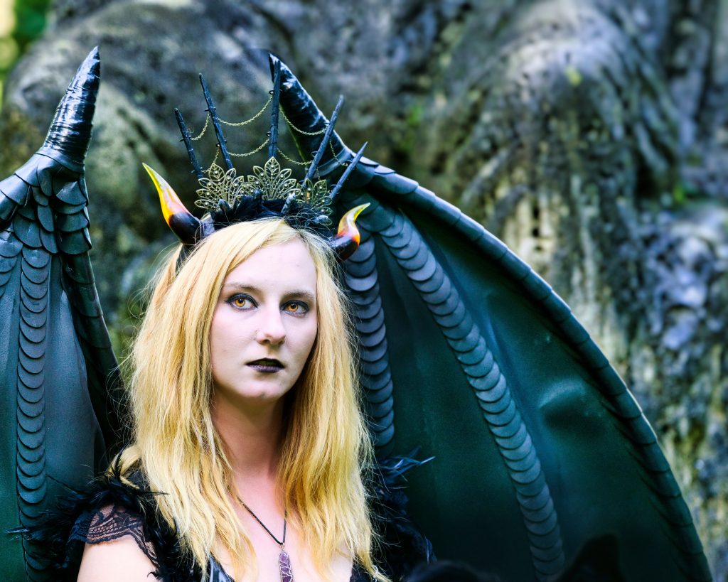 Fantasy-Porträt einer Frau mit schwarzen Flügeln, Krone und dunklem Make-up – eindrucksvolle und stimmungsvolle Fantasy Fotografie im Freien.