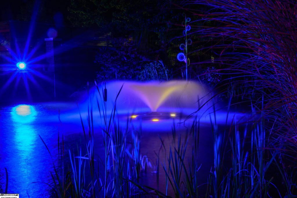 Langzeitbelichtung eines farbig beleuchteten Springbrunnens bei Nacht – kreative Landschaft Fotografie mit Lichteffekten.