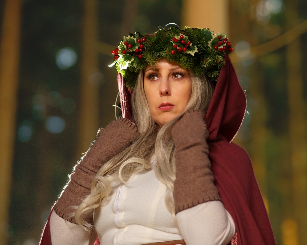 Frau in Fantasy-Kleidung mit Kapuze und winterlichem Kranz aus Tannengrün und Beeren im Wald