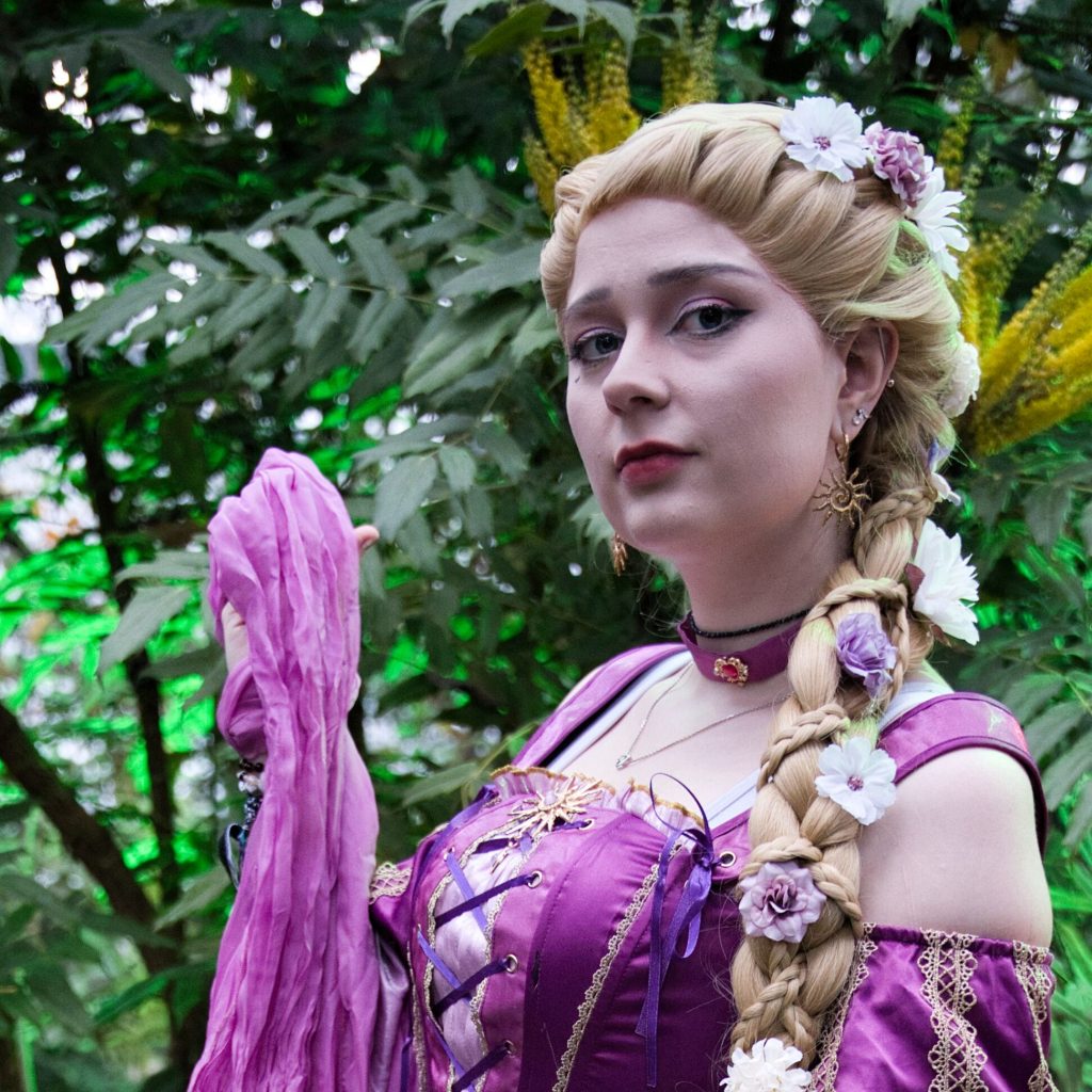 Fantasyporträt einer Frau im violetten Kleid mit geflochtenem Haar und Blumen, stehend in dichter grüner Vegetation