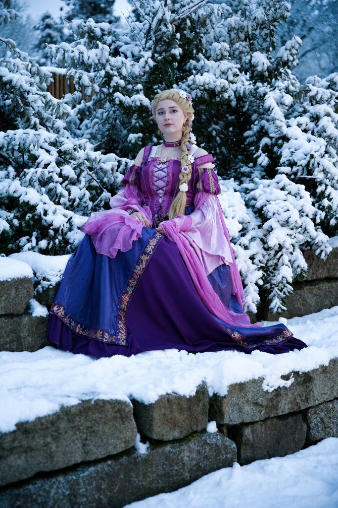 Fantasyporträt einer Frau in violettem Kleid, sitzend auf einer Steinmauer in verschneiter Winterlandschaft