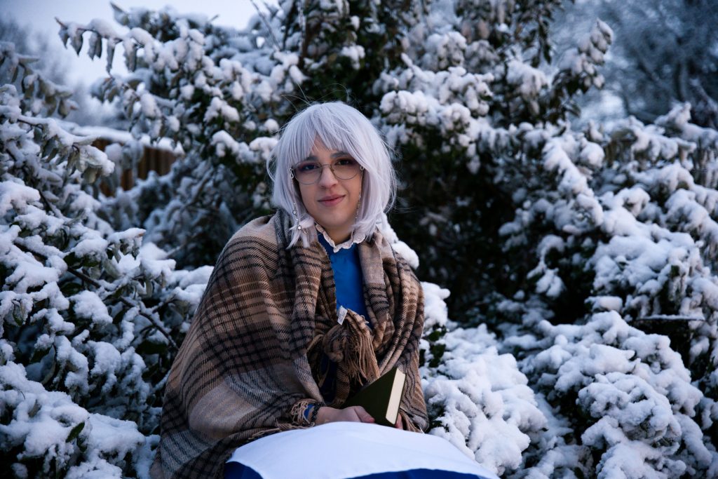 Fantasy-Fotografie einer Frau mit weißem Haar und Buch in verschneiter Winterlandschaft: