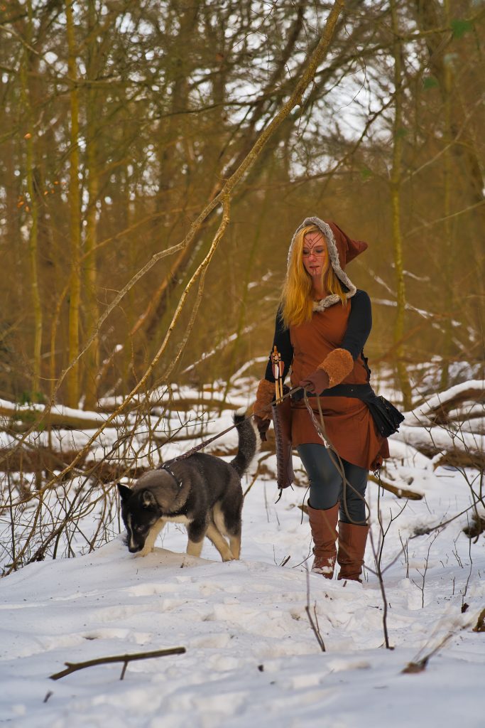 Fantasy-Fotografie einer Kriegerin mit Runen-Gesichtsbemalung und Husky auf einem verschneiten Waldpfad – mystische Szene von Schwarz Fotografien