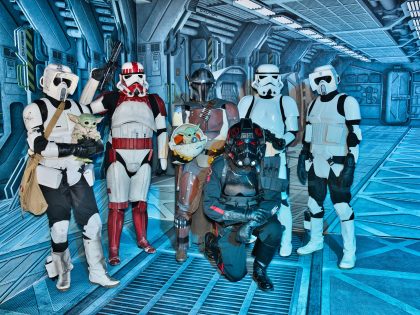 Gruppe von Star-Wars-Cosplayern in Rüstungen posiert in Raumschiff-Kulisse mit Grogu-Figuren.