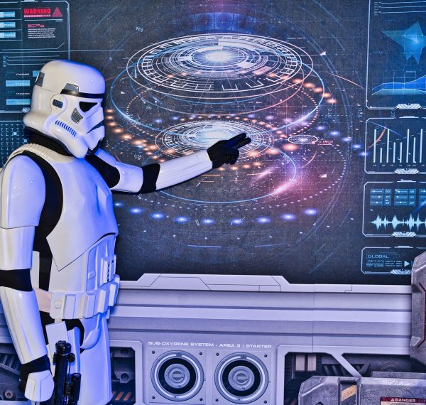 Stormtrooper in weißer Rüstung zeigt auf holografisches Galaxie-Display mit futurativen Elementen. Thematisch passend zum Thema Cosplay Fotografie.